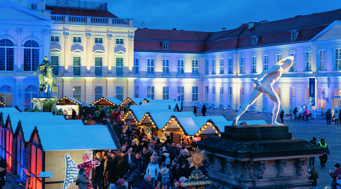 Charlottenburg Palace Christmas market at night time with the palace in the background, a statue in the foreground with market stalls and people browsing.